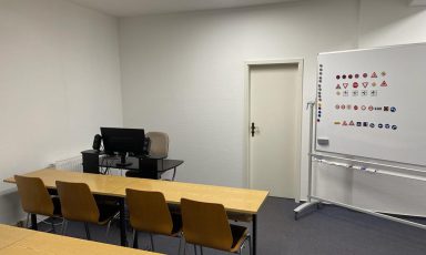 Fahrschule Rottweil mit Tischen, Stühlen, einem Computer und einer Tafel mit Verkehrsschildern.